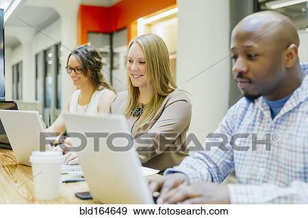 Business people working on laptops in office meeting View Large Photo Image Stock Photo - Business people working on laptops in office meeting. Fotosearch