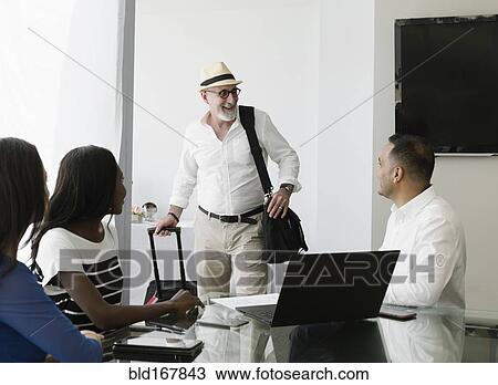 Stock Image - Businessman greeting colleagues in office meeting. Fotosearch