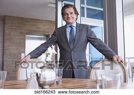 Stock Image - Businessman standing at dining table. Fotosearch