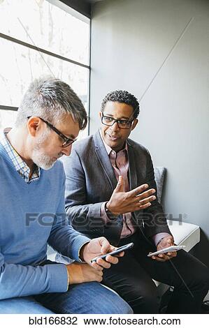 Stock Image - Businessmen using cell phones in office lobby. Fotosearch