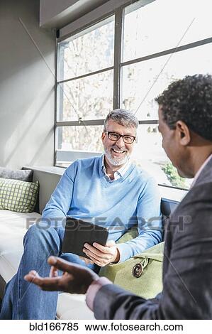 Stock Photography - Businessmen using digital tablet in office lobby. Fotosearch