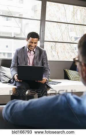 Stock Image - Businessmen using laptop in office lobby. Fotosearch