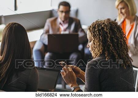 Picture - Businesswoman using cell phone in office meeting. Fotosearch
