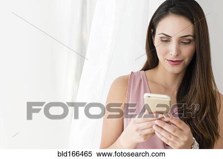 Stock Photography - Businesswoman using cell phone near curtain. Fotosearch