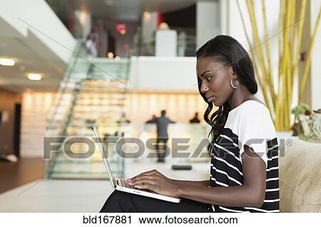 Stock Image - Businesswoman using laptop in hotel lobby. Fotosearch