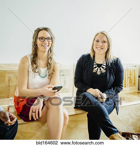 Businesswomen holding cell phones in office lobby View Large Photo Image Stock Image - Businesswomen holding cell phones in office lobby. Fotosearch