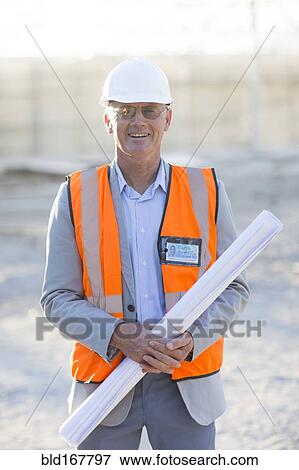 Stock Photo - Caucasian architect holding blueprints at construction site. Fotosearch