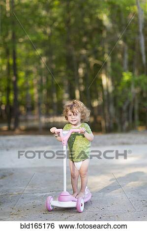 Stock Photograph - Caucasian baby boy riding scooter on dirt path. Fotosearch
