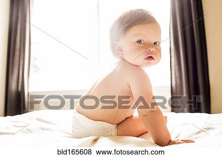 Stock Photo - Caucasian baby girl sitting on bed. Fotosearch
