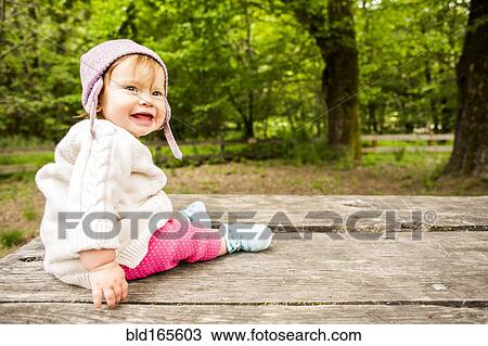 Stock Image - Caucasian baby girl sitting on picnic table in forest. Fotosearch