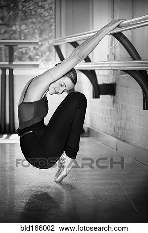 Stock Image - Caucasian ballet dancer stretching at barre in studio. Fotosearch