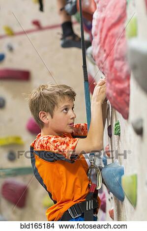 Picture - Caucasian boy climbing rock wall indoors. Fotosearch