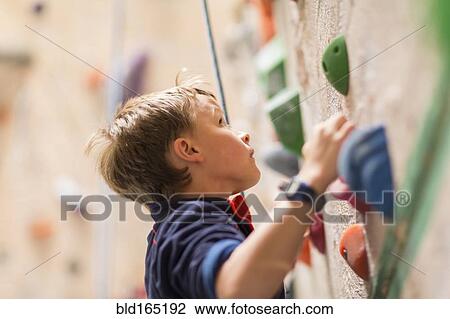Stock Image - Caucasian boy climbing rock wall indoors. Fotosearch
