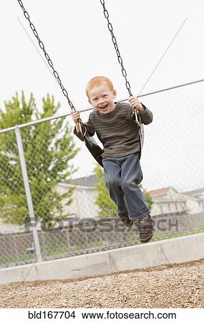 Picture - Caucasian boy sitting on playground swing. Fotosearch