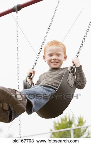 Stock Image - Caucasian boy sitting on playground swing. Fotosearch