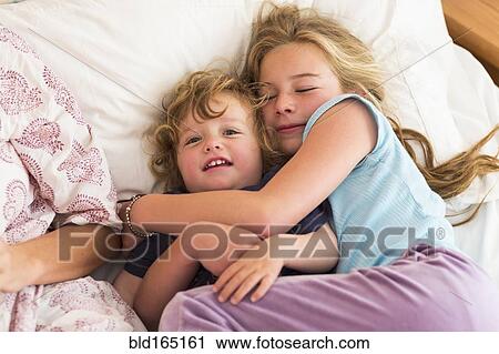 Stock Image - Caucasian brother and sister cuddling on bed. Fotosearch