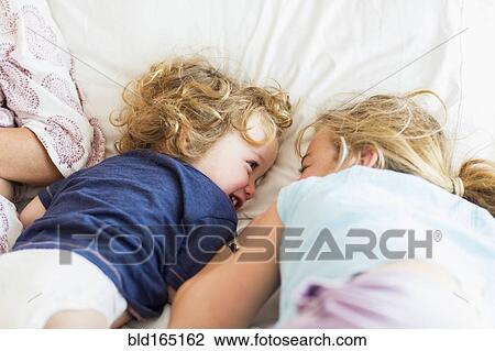 Stock Image - Caucasian brother and sister playing on bed. Fotosearch