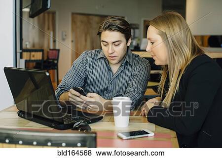 Stock Photo - Caucasian business people using cell phone in cafe. Fotosearch