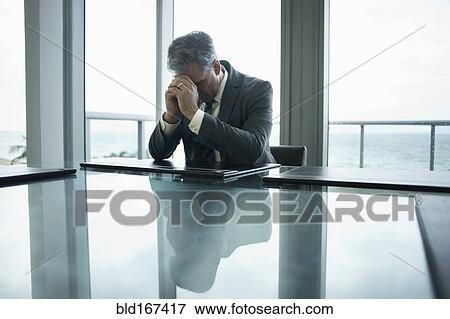 Stock Photo - Caucasian businessman holding head in hands at conference table. Fotosearch