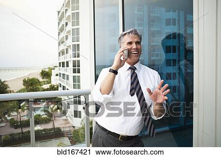 Stock Image - Caucasian businessman talking on cell phone on balcony. Fotosearch