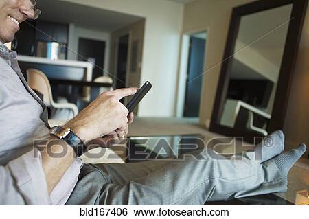 Stock Photograph - Caucasian businessman using cell phone in hotel room. Fotosearch