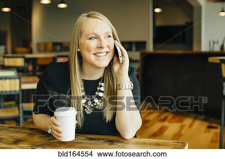 Picture - Caucasian businesswoman talking on cell phone in cafe. Fotosearch