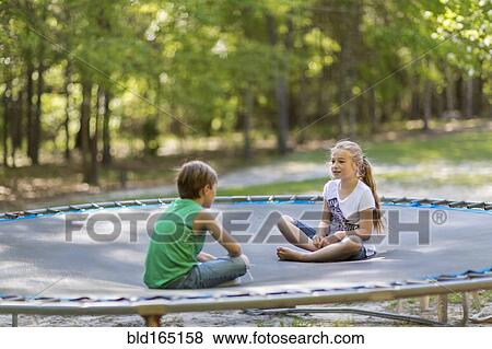 Stock Photo - Caucasian children sitting on trampoline. Fotosearch