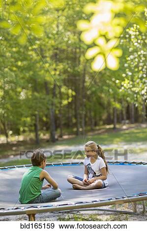 Stock Photo - Caucasian children sitting on trampoline. Fotosearch