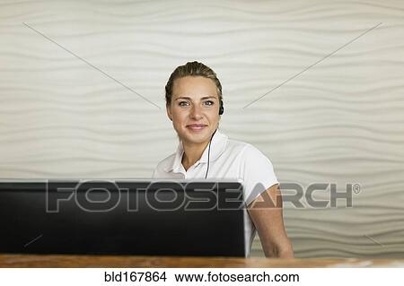 Picture - Caucasian concierge smiling behind hotel front desk. Fotosearch