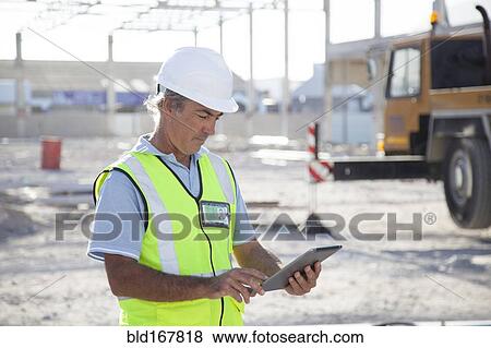 Stock Photo - Caucasian construction worker using digital tablet at construction site. Fotosearch