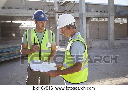 Stock Photograph - Caucasian construction workers talking at construction site. Fotosearch