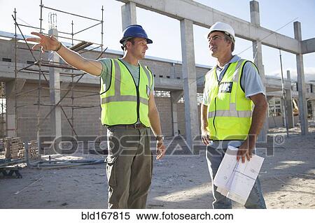 Stock Photography - Caucasian construction workers talking at construction site. Fotosearch