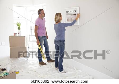 Stock Image - Caucasian couple hanging picture in new home. Fotosearch