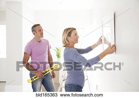 Caucasian couple hanging picture in new home View Large Photo Image Stock Image - Caucasian couple hanging picture in new home. Fotosearch