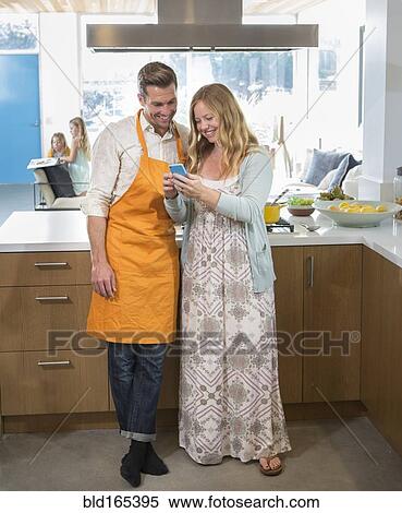 Stock Photography - Caucasian couple using cell phone in kitchen. Fotosearch