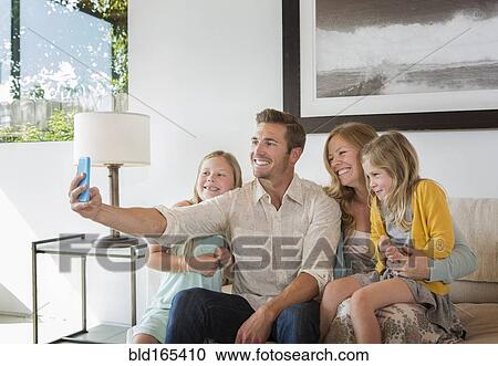 Stock Image - Caucasian family taking selfie on sofa. Fotosearch