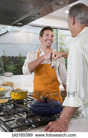 Stock Photo - Caucasian father and son fist-bumping in kitchen. Fotosearch