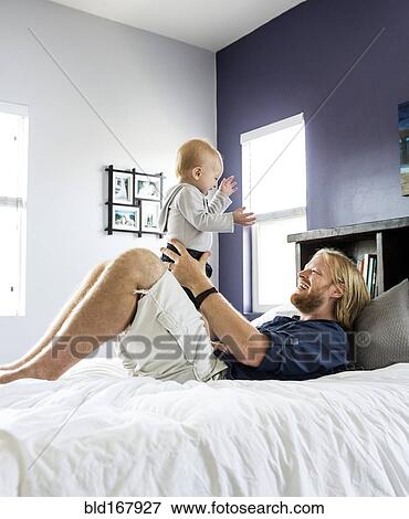 Stock Photo - Caucasian father and son playing on bed. Fotosearch