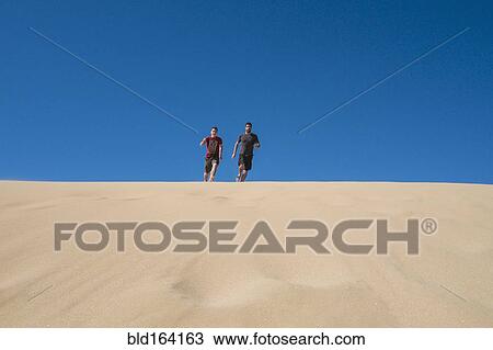 Stock Image - Caucasian father and son running on sand dune. Fotosearch