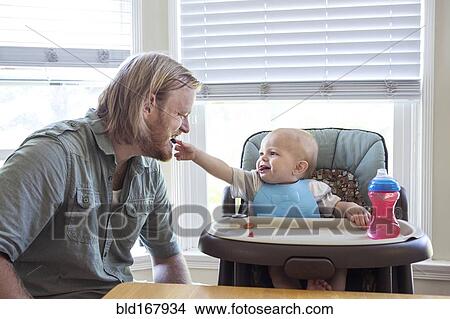 Picture - Caucasian father feeding son in high chair. Fotosearch