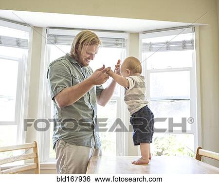 Caucasian father teaching son to stand on table View Large Photo Image Stock Photograph - Caucasian father teaching son to stand on table. Fotosearch