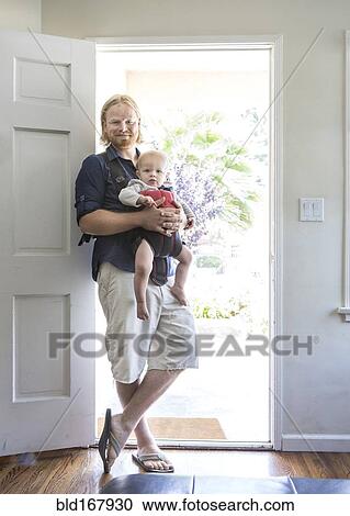 Stock Image - Caucasian father wearing son in harness in doorway. Fotosearch