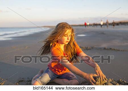 Picture - Caucasian girl building sandcastle on beach. Fotosearch