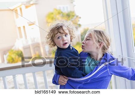 Stock Photo - Caucasian girl carrying baby brother on porch. Fotosearch