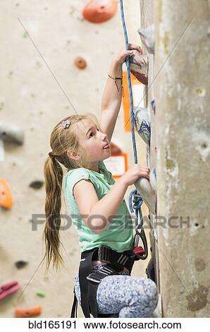 Stock Image - Caucasian girl climbing rock wall indoors. Fotosearch