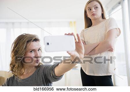 Caucasian girl embarrassed of mother taking selfies with cell phone View Large Photo Image Stock Photograph - Caucasian girl embarrassed of mother taking selfies with cell phone. Fotosearch