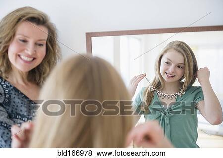 Stock Photo - Caucasian girl examining necklace in mirror with mother. Fotosearch