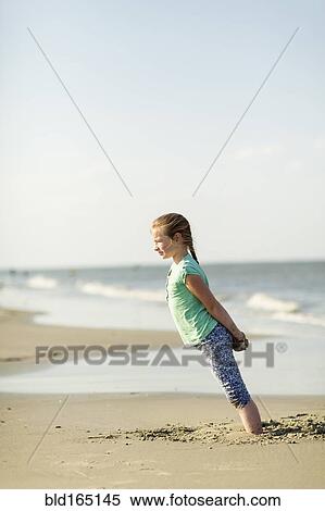 Stock Photography - Caucasian girl leaning in sand on beach. Fotosearch