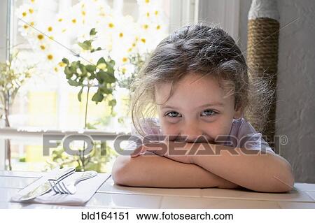 Stock Image - Caucasian girl leaning on kitchen table. Fotosearch