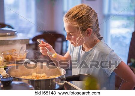 Stock Photo - Caucasian girl tasting food and cooking in kitchen. Fotosearch